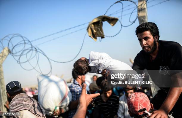 Syrian man fleeing the war passes a child over border fences to enter Turkish territory illegally, near the Turkish border crossing at Akcakale in...