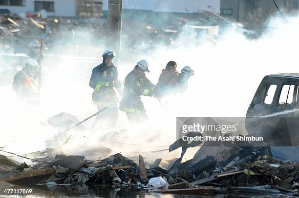 Fire fighters rescue a woman from smoke raising Natori city a day after the magnitude 9.0 strong earthquake and subsequent tsunami struck on March...