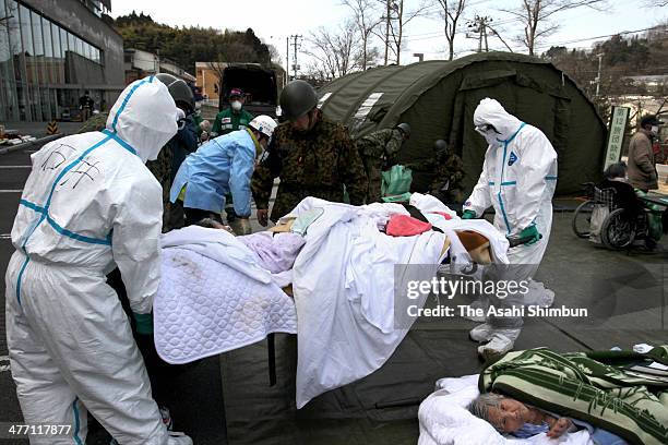 Staffs wearing radiation protection gears carry possible radiation exposed patients at an evacuation center after Fukushima Daiichi Nuclear Power...