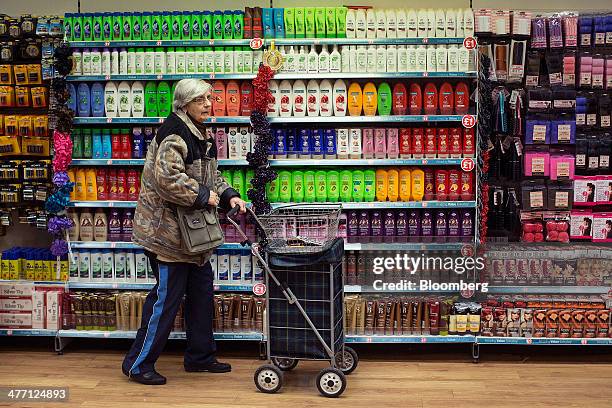 Customer pushes a shopping trolley past a display of hair-care products inside a Poundland discount store, operated by Poundland Group Plc in London,...