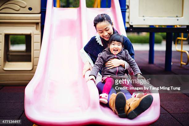 Mom & toddler girl sliding joyfully in playground