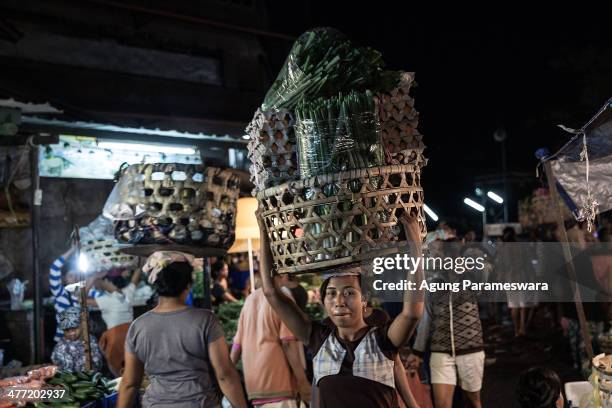 An Indonesian female porter carries a basket of vegetables and eggs on her head at Badung traditional market on March 8, 2014 in Denpasar, Bali,...