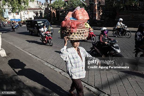 An Indonesian female porter carries a basket of fruit, vegetables and dry goods on her head at Badung traditional market on March 8, 2014 in...