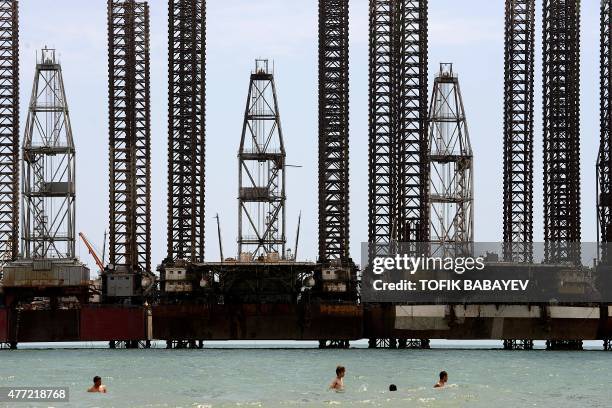 Boys cool off in the Caspian Sea, with offshore oil rigs seen in the background, in Baku on June 15, 2015. AFP PHOTO / TOFIK BABAYEV