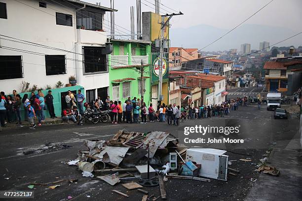 Refuse from a barricade put up by protesters clutters the street in front of a long queue to buy basic foodstuffs at a supermarket before sunrise on...