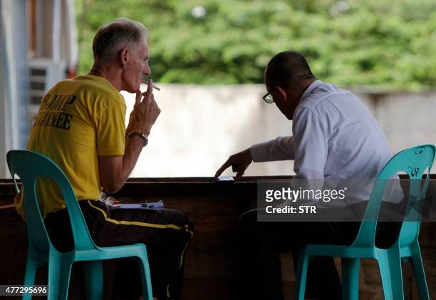 Peter Scully of Australia , accused of raping and trafficking two girls in the Philippines, smokes a cigarette as he confers with his lawyer outside...
