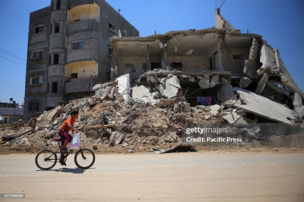 A Palestinian boy rides his bicycle past the rubble of...