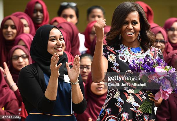 First Lady Michelle Obama gestures and holds flowers as she is received by young students holding the American flag in the courtyard before an event...