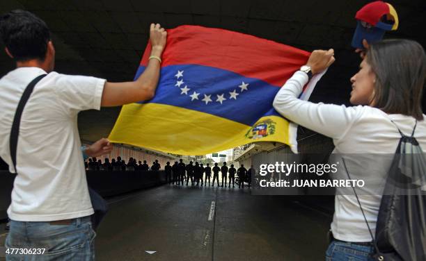 Demonstrators show a Venezuelan national flag to riot police during a protest against the government of Venezuelan President Nicolas Maduro in...