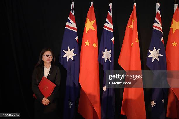 Woman holding a copy of the Free Trade Agreement stands next to National flags of China and Australia during a signing ceremony on June 17, 2015 in...