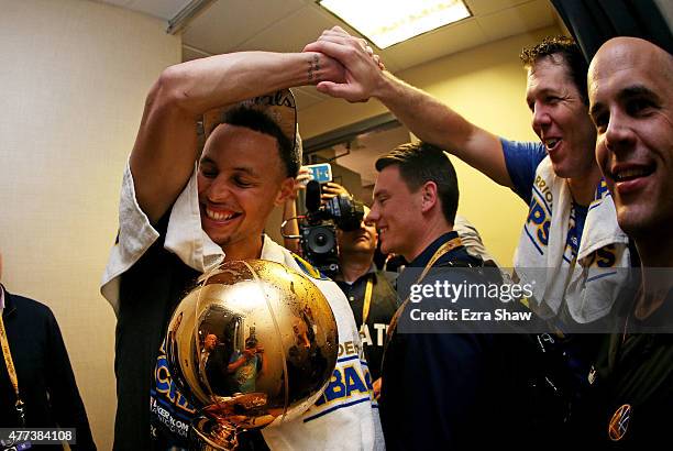 Stephen Curry of the Golden State Warriors celebrates with assistant coach Luke Walton and the Larry O'Brien NBA Championship Trophy in the locker...