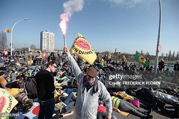 Man holds a burning flare as French and German anti-nuclear activists lay on the ground as they take part in a protest against the nuclear powerplant...