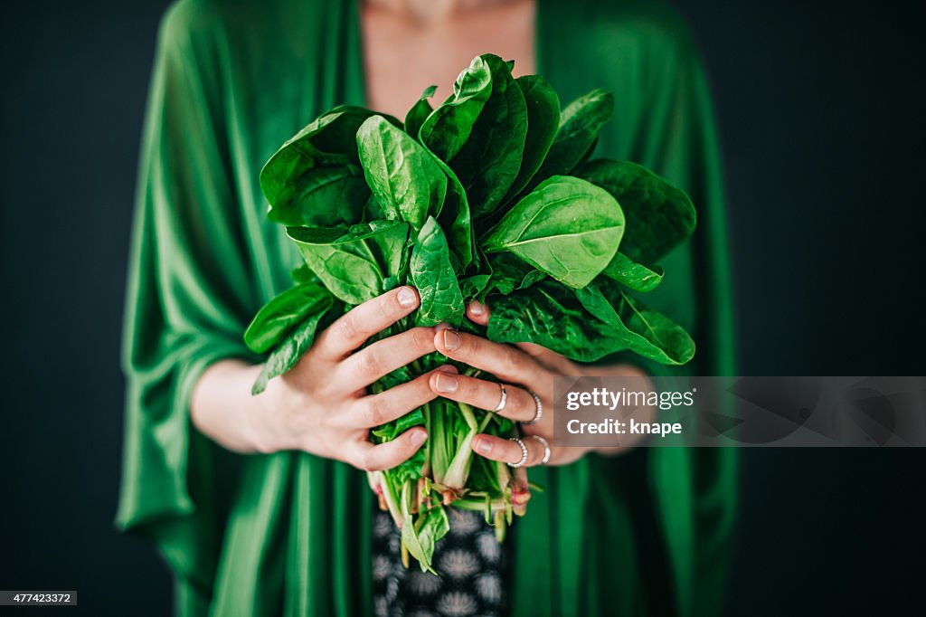 Young woman holding spinach leafs salad