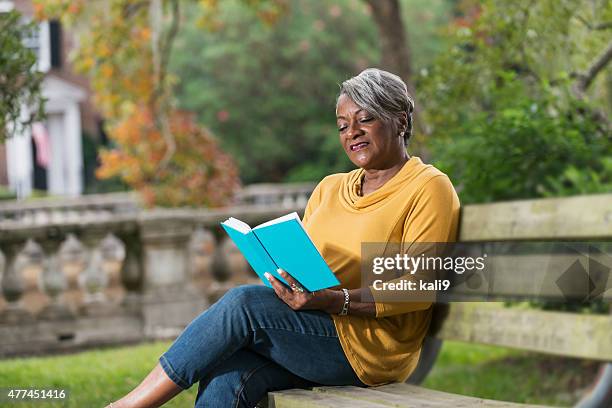 senior mujer leyendo un libro negro - mujer leyendo libro en el parque fotografías e imágenes de stock