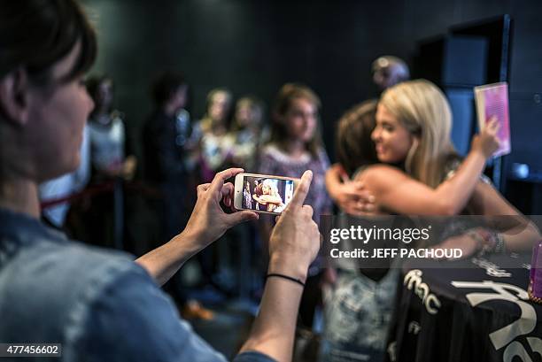 French blogger Marie Lopez, aka EnjoyPhoenix, gives a hug to a fan as another woman is taking a picture of them during a signing of her first book...