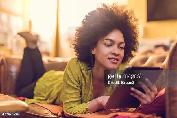african american woman reading something from e-reader at home. - e reader stockfoto's en -beelden