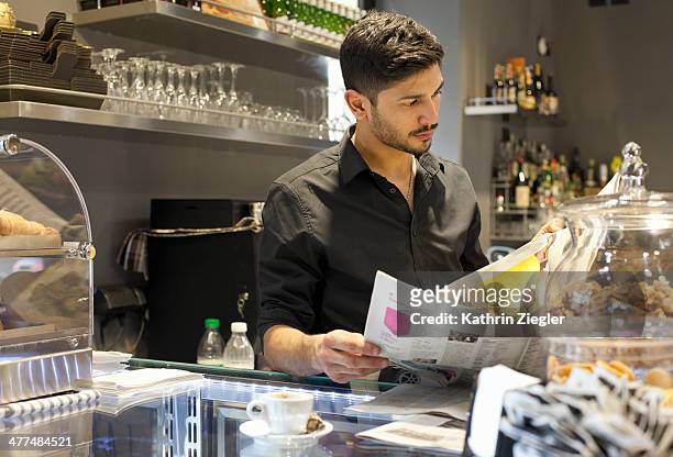 barista taking a break, reading the paper - junger mann liest zeitung stock-fotos und bilder