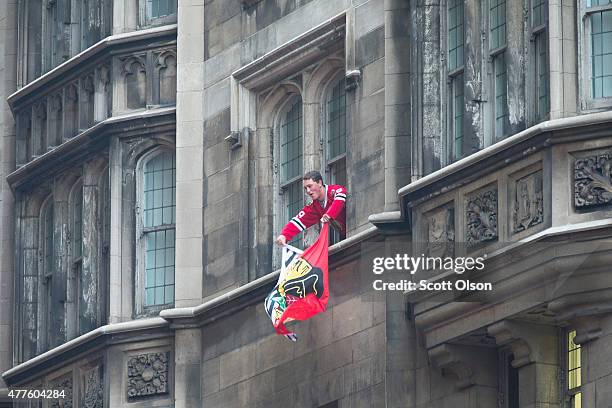 Fan waves a Blackhawks flag from a building as people pack the streets below to watch a parade held to celebrate the Chicago Blackhawks' winning of...