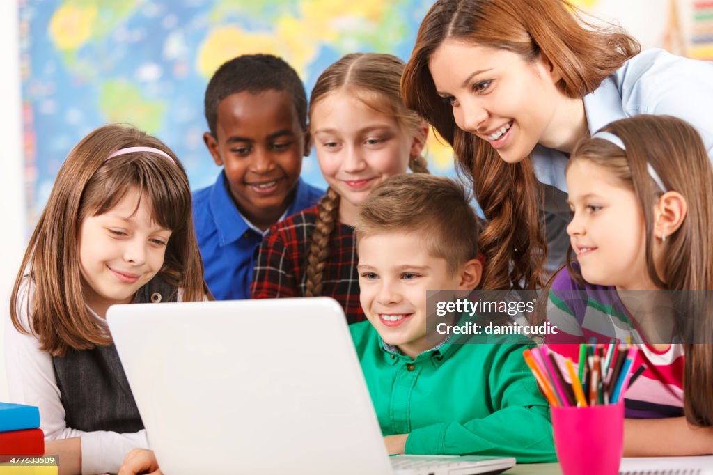 School children using laptop with teacher in the classroom