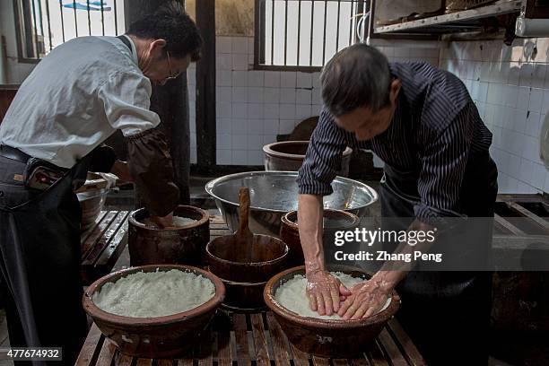 In a traditional workshop, craftsmen are filling cooked rice into terrines, where the rice will be fermented to rice wine. Rice wine, also known as...