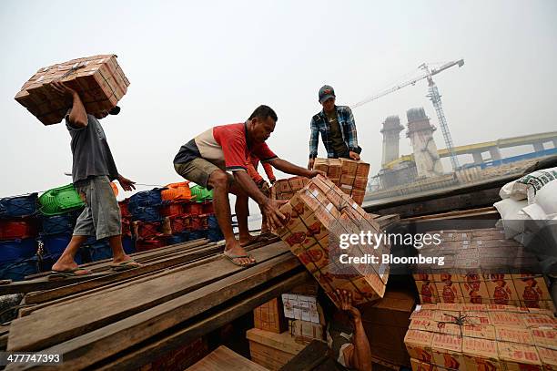 Laborers load goods onto a boat as a new bridge stands under construction across the Siak river in Pekanbaru, Riau Province, Indonesia on Friday,...