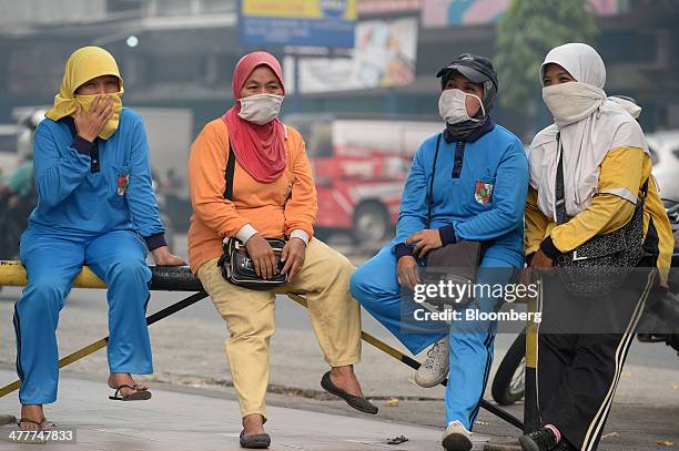 Women wearing masks sit by the side of a road in downtown Pekanbaru, Riau Province, Indonesia on Friday, March 7, 2014. Indonesian central bank...