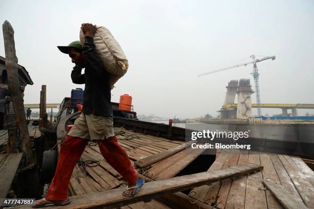 Laborer unloads goods from a boat as a new bridge stands under construction across the Siak river in Pekanbaru, Riau Province, Indonesia on Friday,...