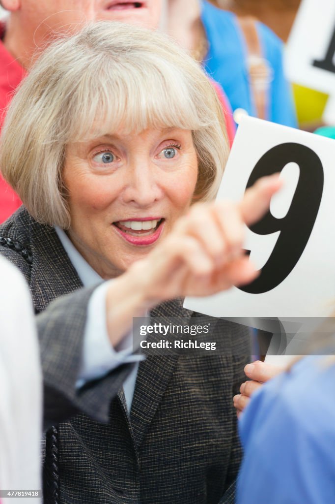 Senior Woman Bidding at a Live Auction