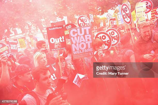 Protesters in central London walk through the haze of a red flare as they demonstrate against austerity and spending cuts on June 20, 2015 in London,...