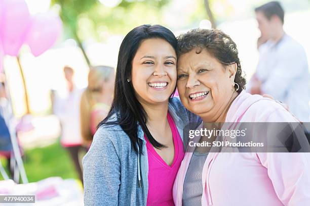 hispanic senior woman and granddaughter attending breast cancer awareness race - mixed race woman stockfoto's en -beelden