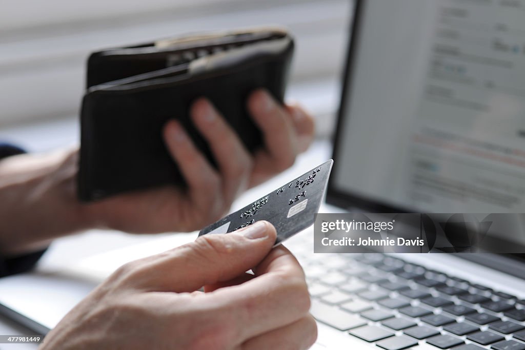 Hand holding credit card and wallet by laptop