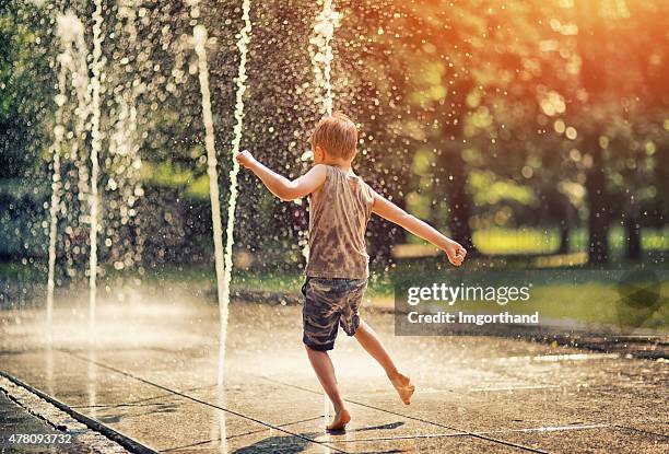 sommer in der stadt – kleiner junge spielt mit brunnen - boy barefoot rear view stock-fotos und bilder