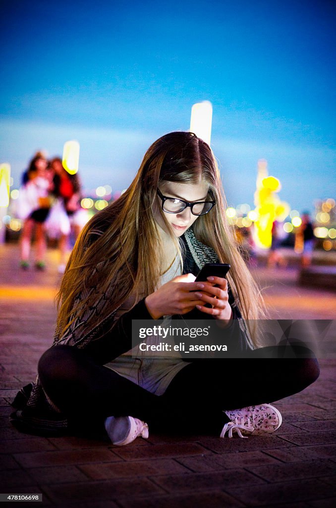 Enviar mensagens de texto a sorrir Jovem mulher com telefone inteligente durante a noite, Tóquio