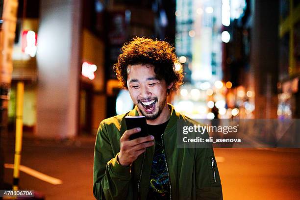 feliz japonés hombre joven con smartphone en la noche, tokyo. - hombre asombrado fotografías e imágenes de stock