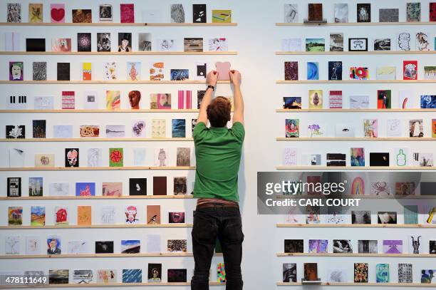Member of staff positions a postcard during the press preview for the original 'secret' art exhibition and sale at the Royal College of Art in London...
