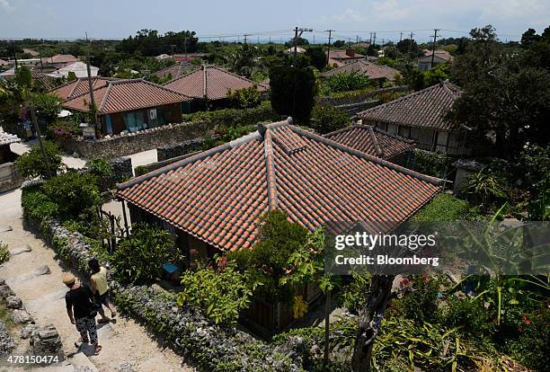 Tourists walk past houses in Taketomi, Okinawa Prefecture, Japan, on Saturday, June 20, 2015. The Abe administration aims to cap increases in...