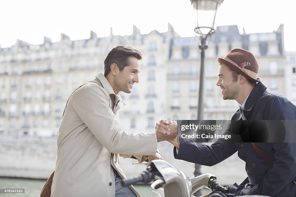 Businessmen shaking hands on bicycles along Seine River, Paris, France