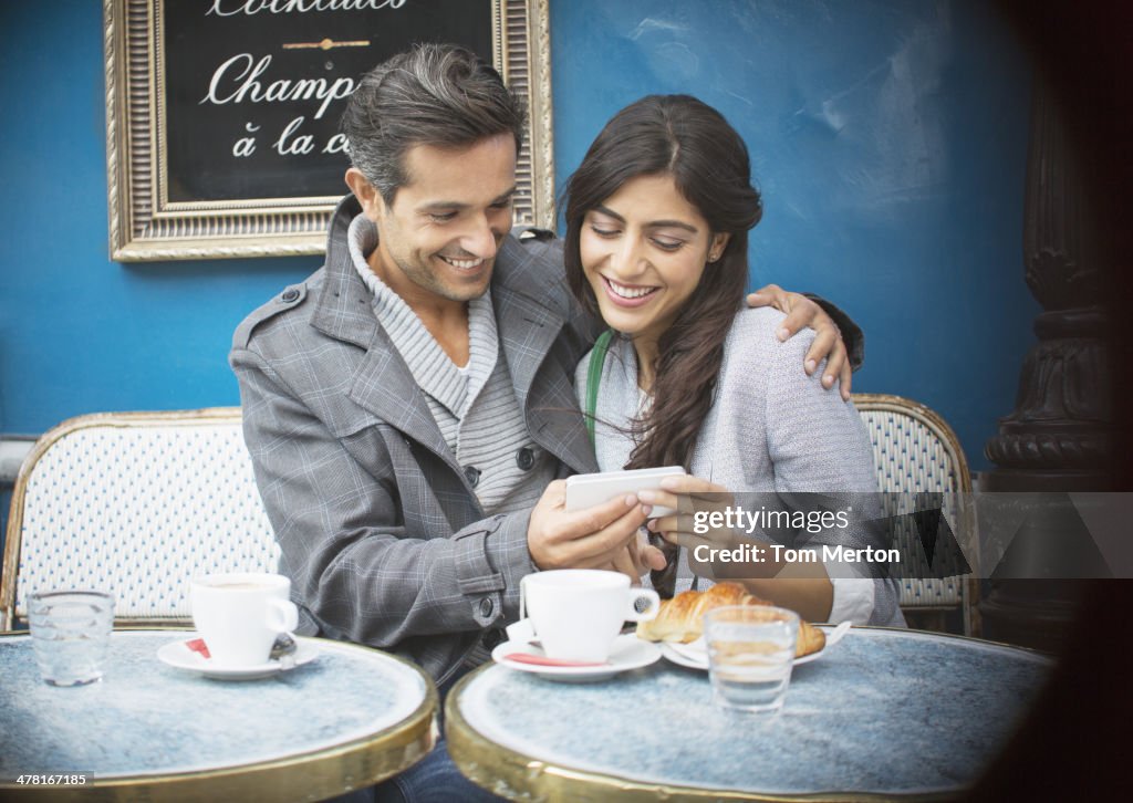 Couple using cell phone at sidewalk cafe, Paris, France