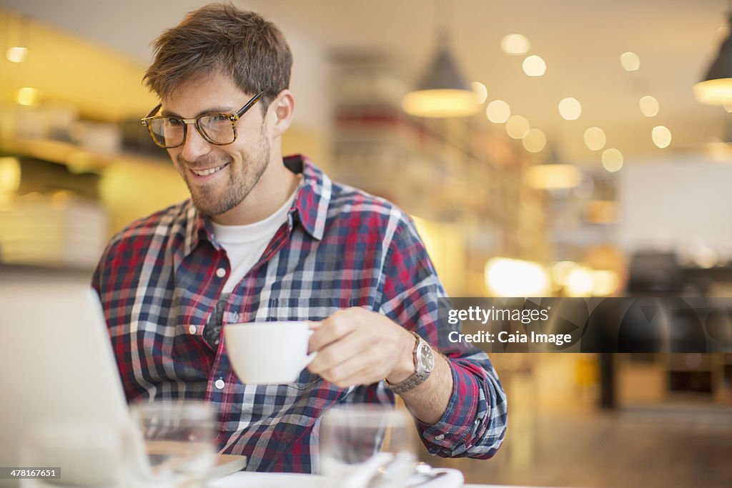 Man using laptop and drinking coffee in cafe