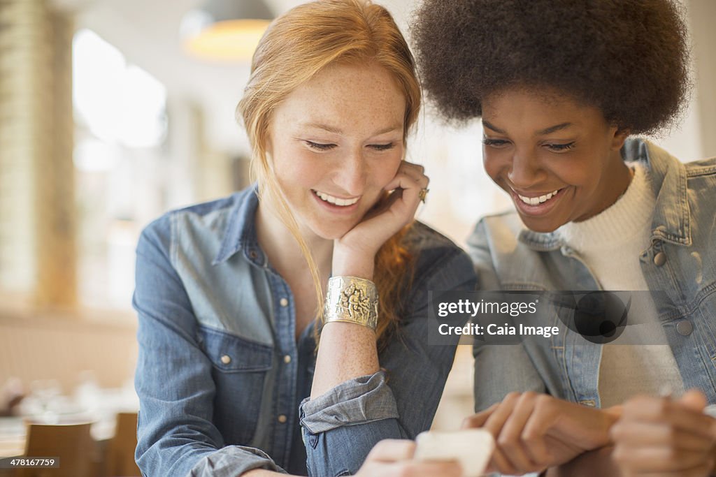 Women using cell phone together in cafe