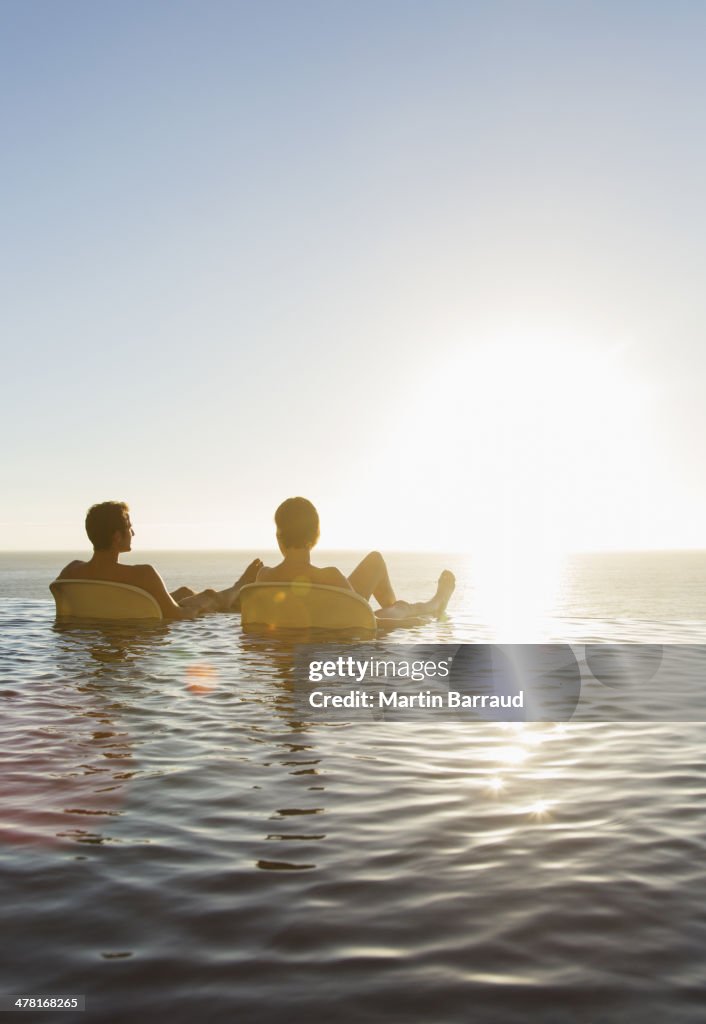 Couple dans les chaises de la pelouse au bord de la piscine à débordement avec vue sur l'océan