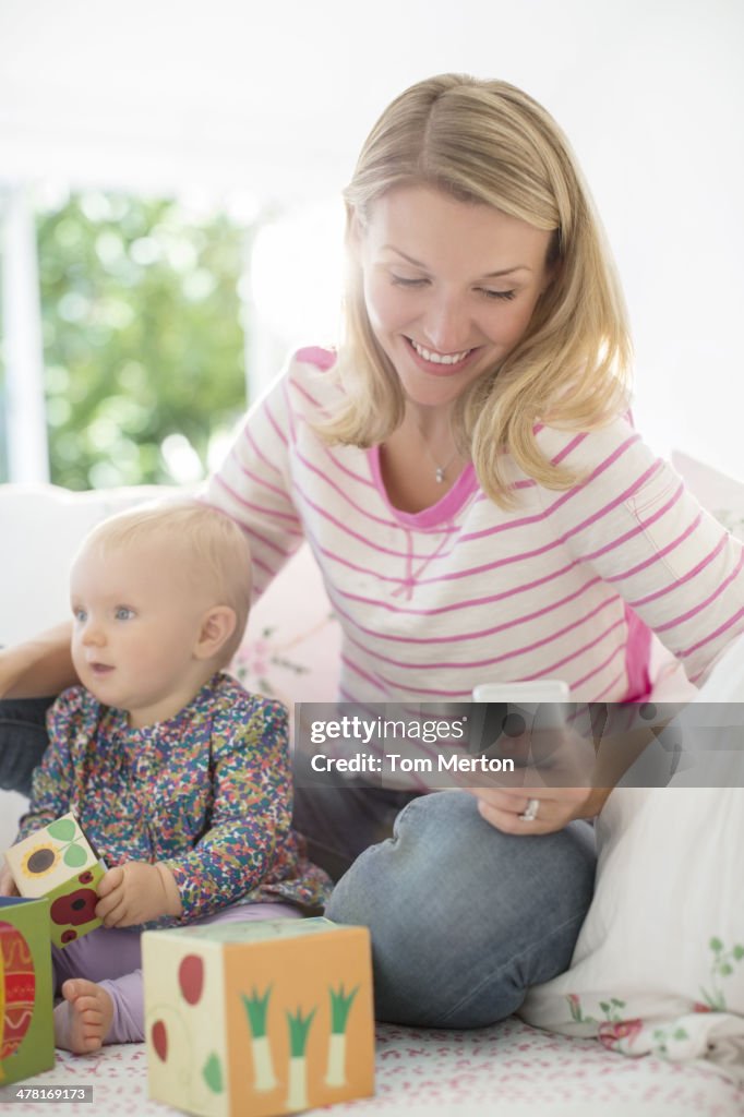 Mother playing with baby girl and checking cell phone