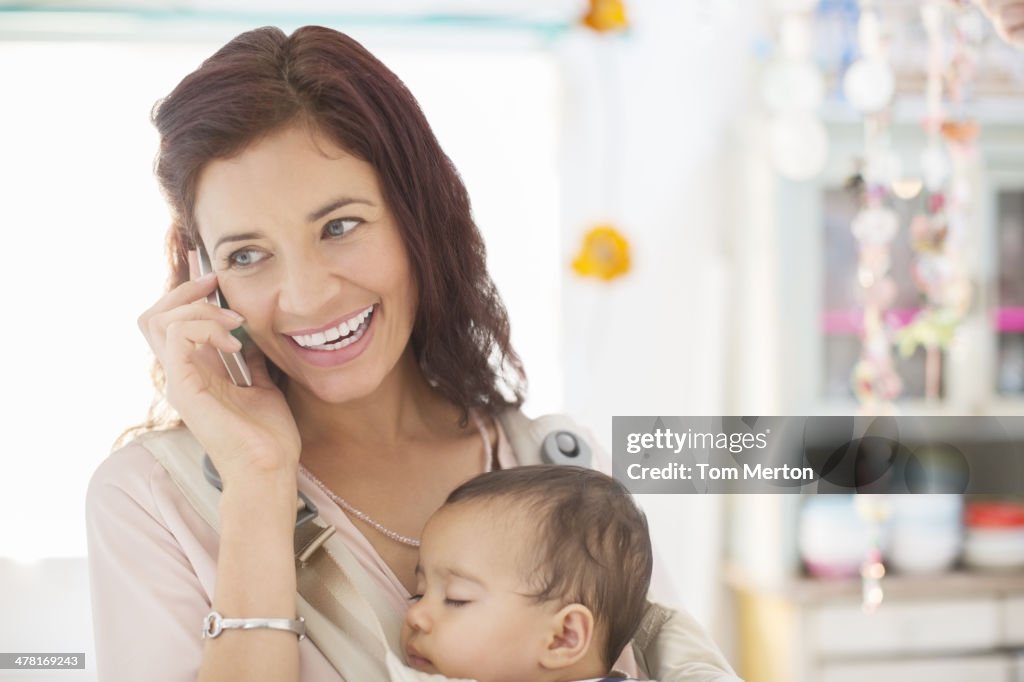 Mother with sleeping baby girl talking on cell phone