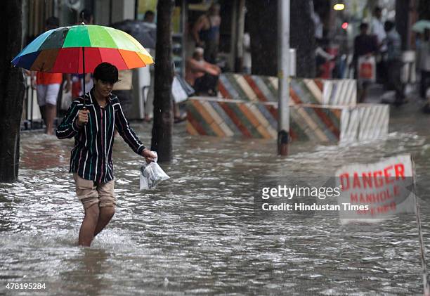 Man walks through a flooded street as a sign read danger after heavy rain at Hindamata, Dadar on June 23, 2015 in Mumbai, India. Heavy rainfall...