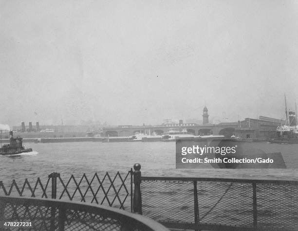 The Erie Lackawanna Railroad and Ferry Terminal , with a clock tower and docked ferries and steamships, as seen from a ship on the Hudson River,...