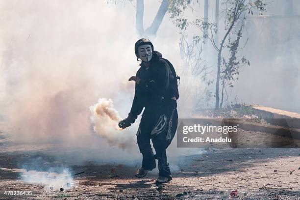 Masked protester throws back a tear gas canister at National Bolivarian Guard members during the anti-government protests in Caracas, Venezuela on...