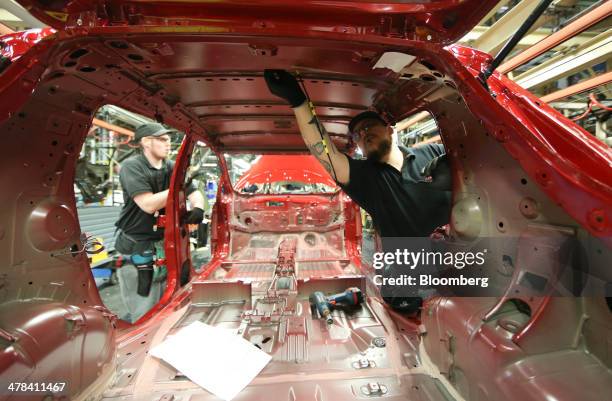 An employee fits parts to the body shell of a new Nissan Leaf automobile as it travels along the production line at Nissan Motor Co.'s vehicle...