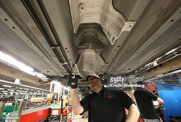 An employee fits a part to the underside of a new Nissan Qashqai automobile as it travels along the production line at Nissan Motor Co.'s vehicle...