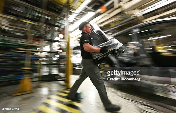 An employee prepares to fit a seat into a new Nissan Qashqai SUV automobile as it travels along the production line at Nissan Motor Co.'s vehicle...