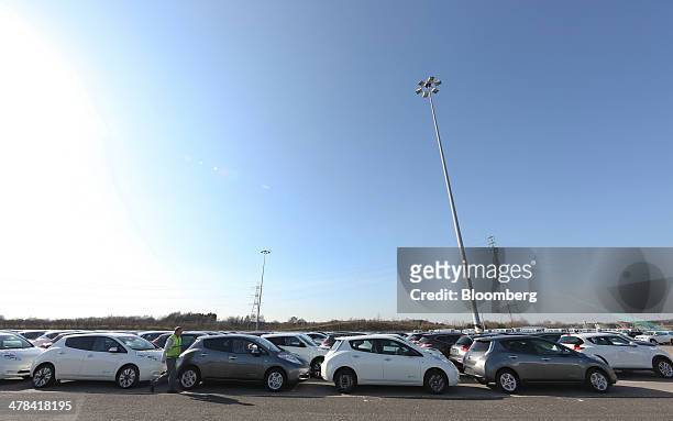 An employee walks past new Nissan Leaf automobiles, produced by Nissan Motor Co., as they stand on the dockside awaiting export at the Port of Tyne,...